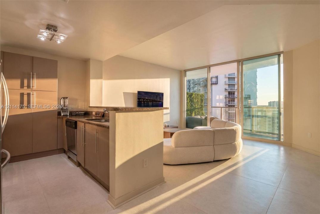 Kitchen featuring flat-panel cabinetry, stone countertops, stainless steel dishwasher, and tile flooring, complete with floor-to-ceiling glass sliding doors opening to a balcony