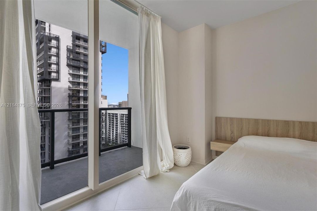 Floor-to-ceiling glass wall, private balcony with metal railing, and wood-finish wall-mounted headboard