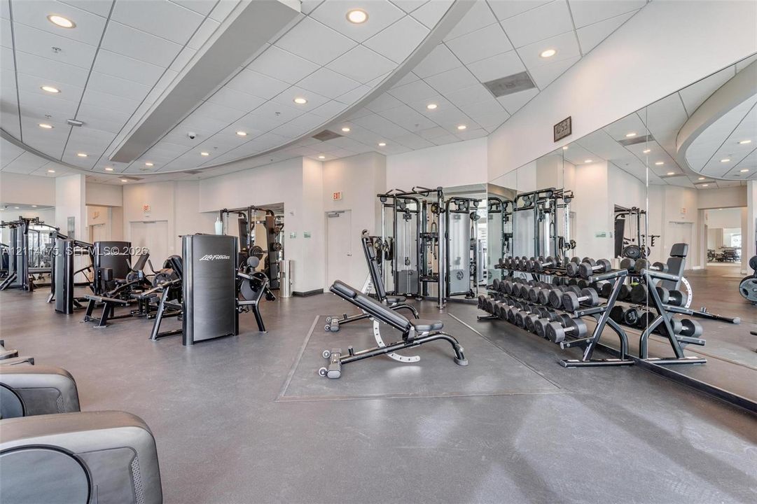 Fitness center featuring recessed lighting, high ceilings with architectural curves, wall-to-wall mirrors, and resilient flooring