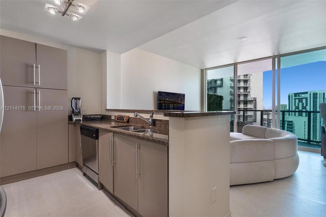 Kitchen featuring flat-panel cabinetry, stone countertops, stainless steel dishwasher, integrated sink with gooseneck faucet, and floor-to-ceiling glass windows