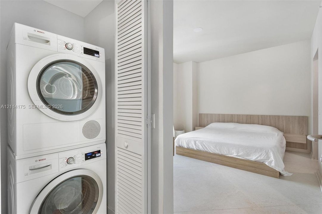 Stacked Bosch laundry unit and louvered closet door featuring a light-toned built-in headboard