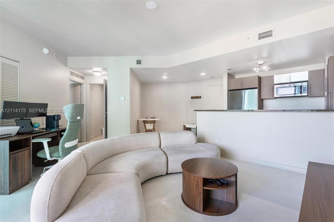 Open floor plan featuring cabinetry with slab-style doors, stone-surface breakfast bar, recessed lighting, and neutral wall-to-wall carpeting