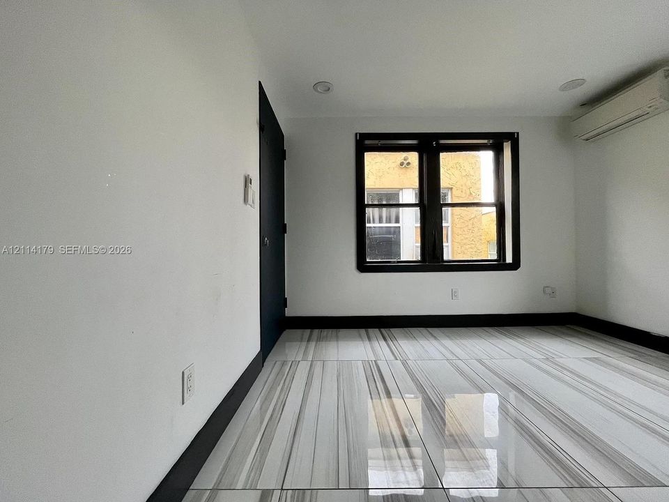 Interior room featuring large-format polished tile flooring, recessed ceiling lighting, a wall-mounted ductless HVAC unit, and a dark-framed window