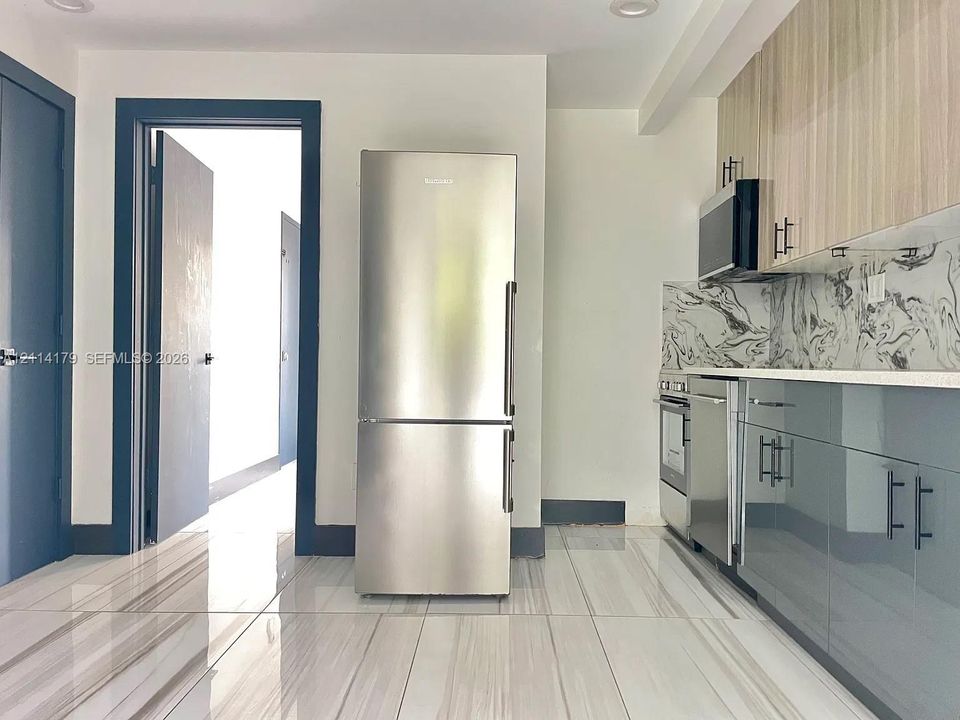 Kitchen featuring high-gloss two-tone cabinetry, stainless steel appliances, patterned stone-style backsplash, and large-format tile flooring