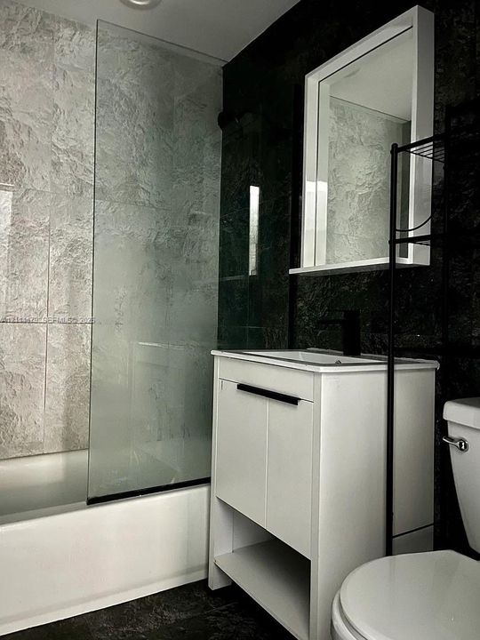 White vanity featuring integrated shelving and a dark-finish faucet, paired with a glass shower screen and dual-tone wall tile detailing