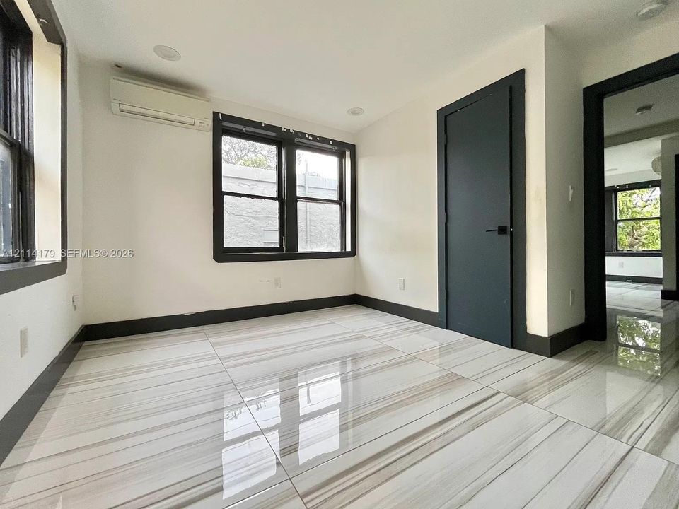 Large-format stone-look tile flooring with high-contrast veining, dark-framed dual-pane windows, recessed ceiling lighting, and a wall-mounted ductless climate control unit