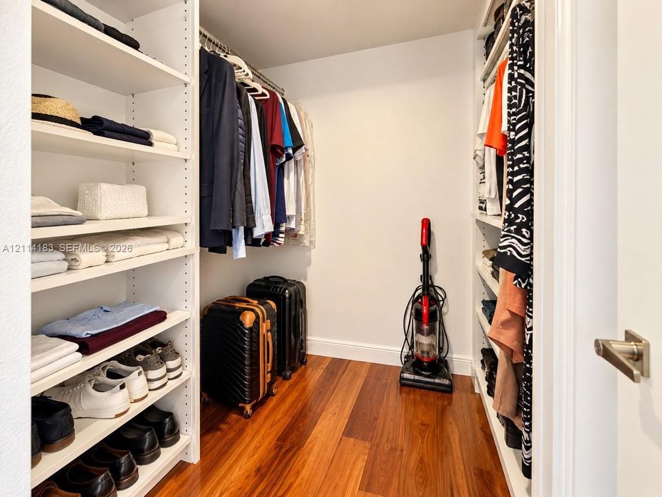 Walk-in closet featuring floor-to-ceiling built-in white shelving, integrated hanging rods, and wood-finish flooring