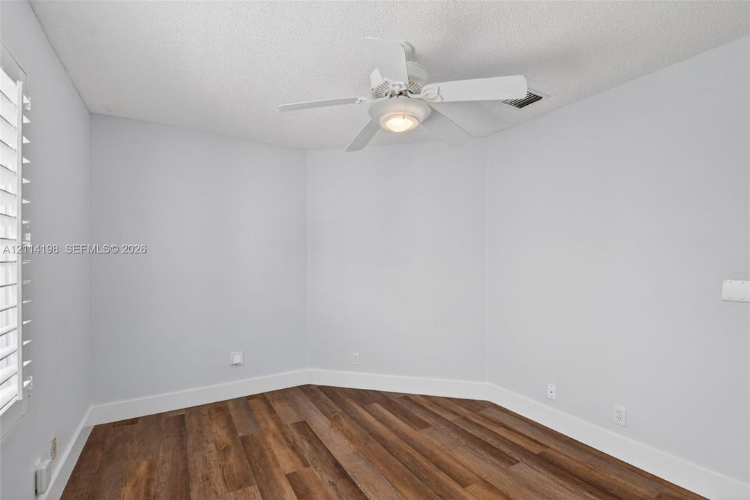 Room featuring wood-finish flooring, white walls, and a ceiling fan with integrated lighting, complemented by shutter-style window coverings