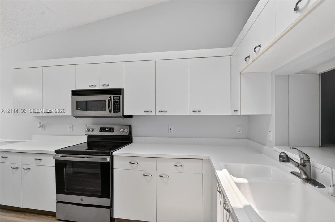 Kitchen featuring white cabinetry, solid-surface countertops, dual-basin sink with pull-down faucet, and stainless steel appliances including a built-in microwave and range