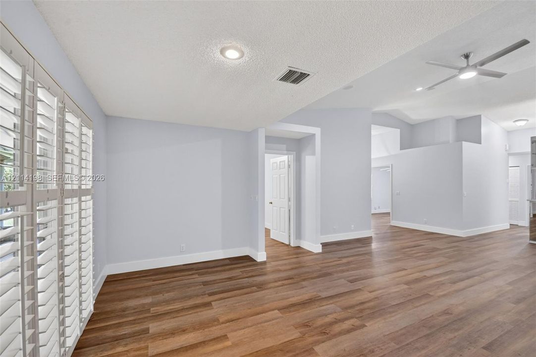 Interior space featuring wood-finish flooring, vaulted ceilings, recessed lighting, a modern ceiling fan, and plantation shutters