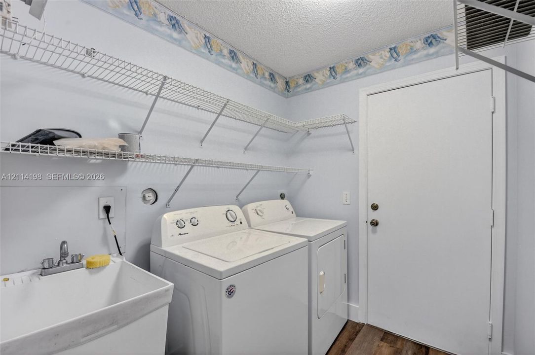 Utility space featuring white wire shelving, a deep utility sink with a chrome faucet, and wood-finish flooring