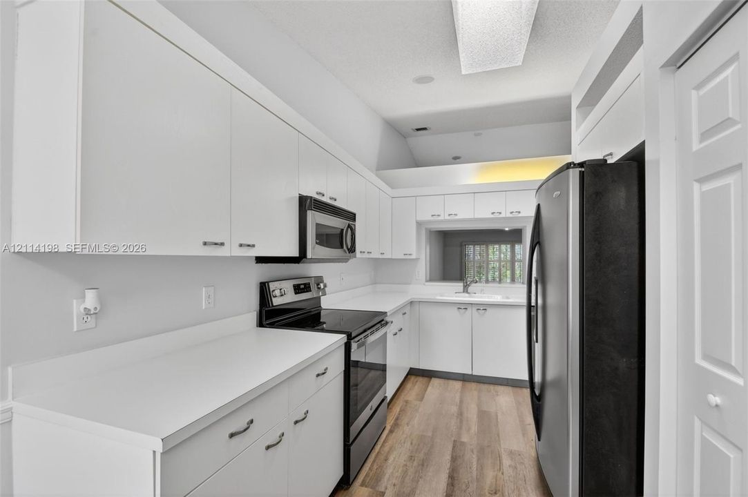 Kitchen featuring white cabinetry, wood-finish flooring, solid surface countertops, and stainless steel appliances