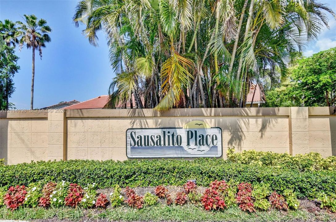 Stucco perimeter wall with integrated signage, manicured shrubbery, and mature palm trees