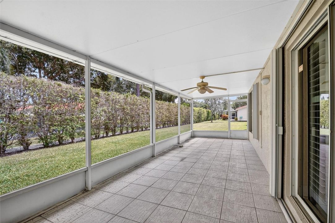 Screened-in porch featuring a solid roof, neutral tile flooring, built-in ceiling fan, and sliding glass door access