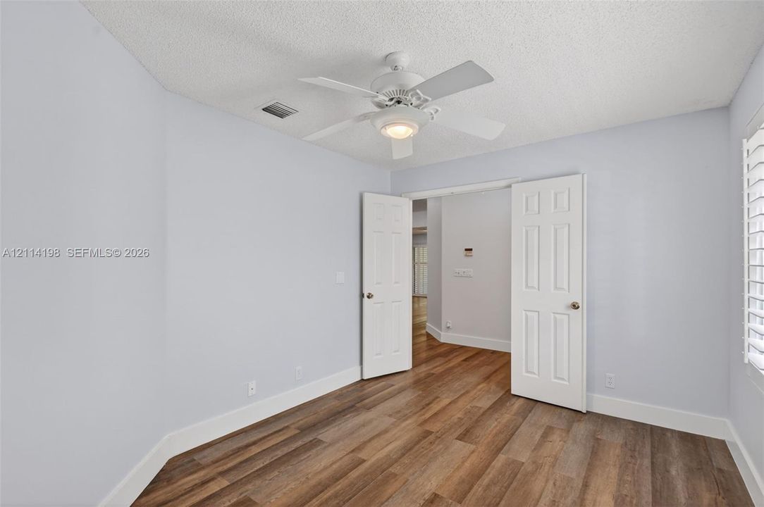 Room featuring wood-finish flooring, white six-panel interior doors, and a ceiling fan with integrated lighting