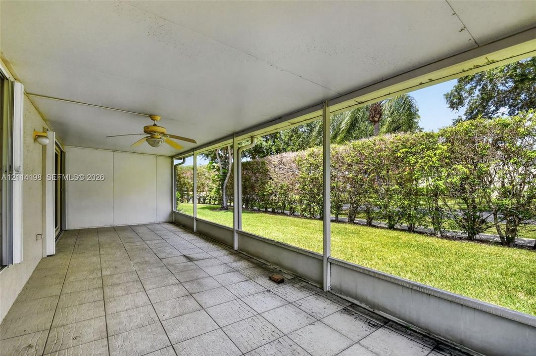 Screened-in porch featuring tile flooring, a ceiling fan, and metal support framing overlooking a manicured lawn and dense perimeter hedge