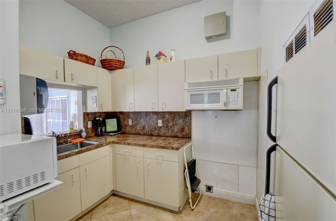 Kitchen area featuring light-toned cabinetry, laminate countertops, a stainless steel sink, tile flooring, and a built-in microwave