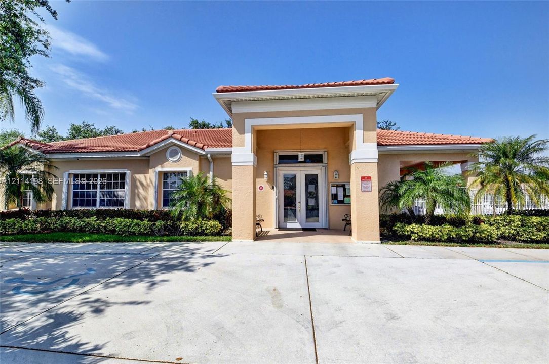 Single-story stucco exterior featuring a clay tile roof, covered entryway with double glass doors, multi-pane windows, and landscaped palms