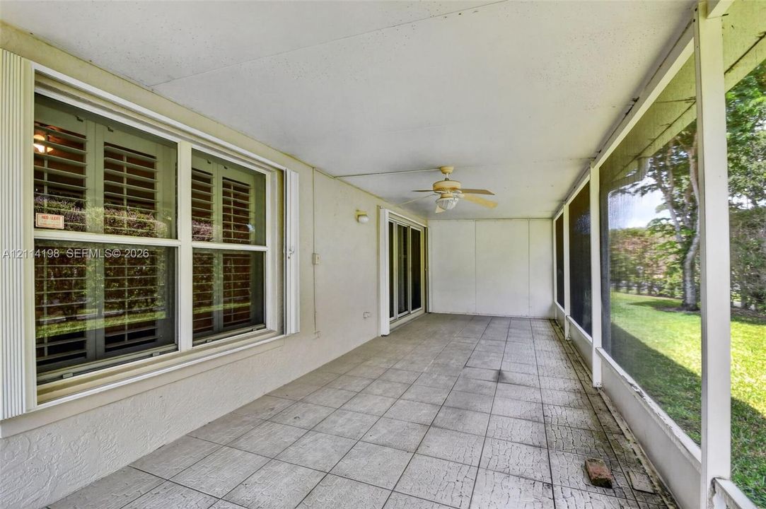 Screened-in porch featuring tile flooring, a ceiling fan, and large windows with integrated shutters