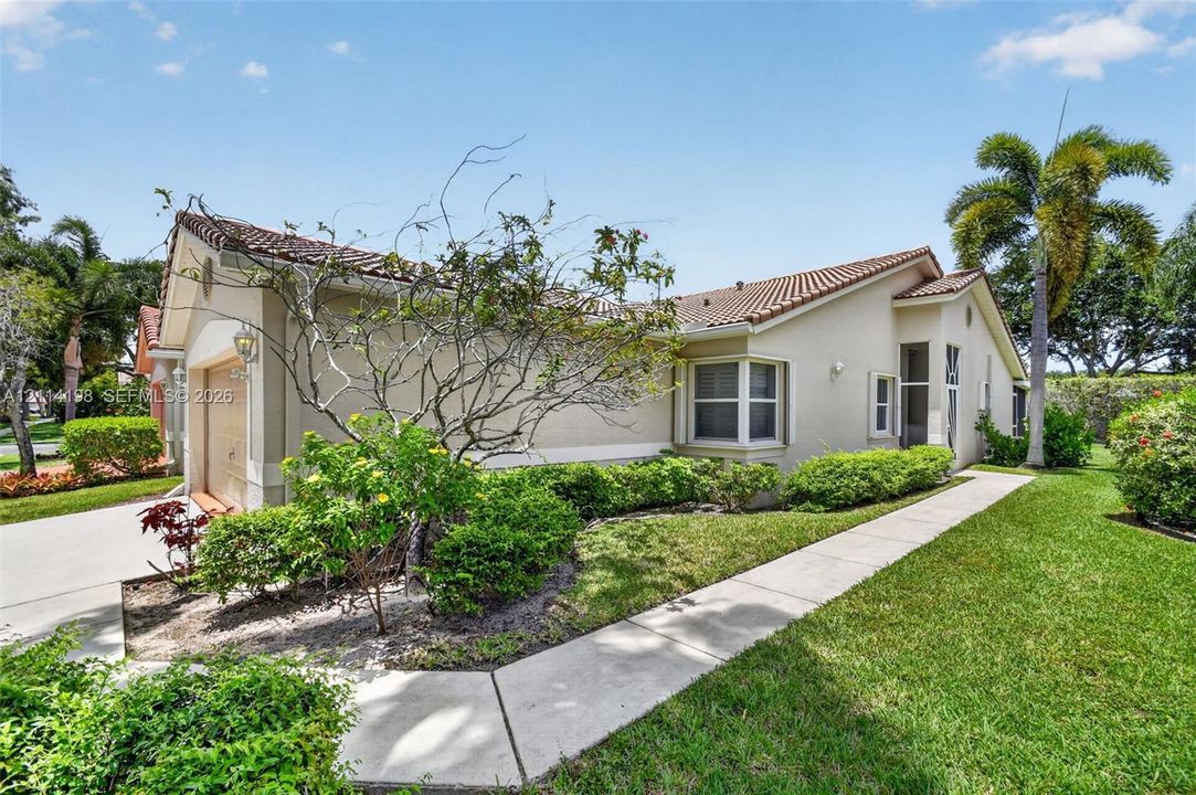Single-story exterior featuring a stucco facade, a tile roof, a two-car garage, and landscaped grounds with a paved walkway