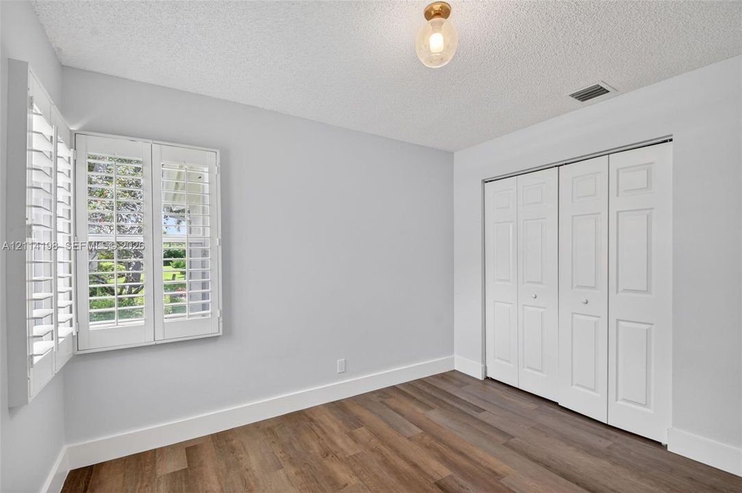 Wood-finish flooring, white plantation shutters, three-panel closet doors, and glass-globe flush mount lighting