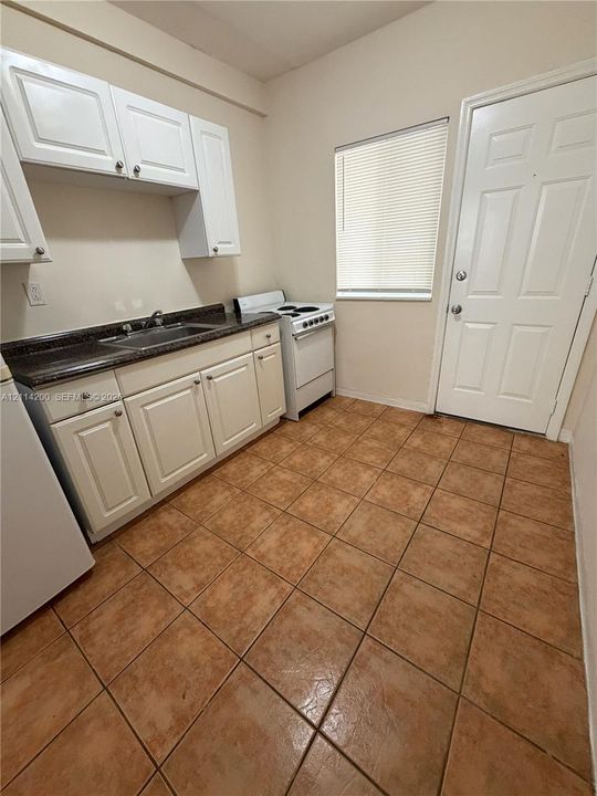 Kitchen featuring white shaker-style cabinetry, dark stone-finish countertops, stainless steel sink with a chrome faucet, and ceramic tile flooring