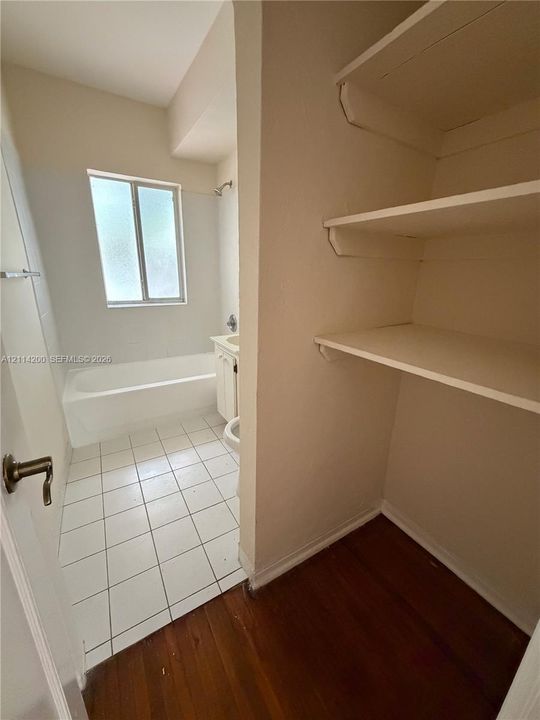 Bathroom featuring a bathtub, single-sink vanity, and white tile flooring, accompanied by an area with wood-finish flooring and built-in shelving