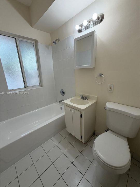 Bathroom featuring a ceramic tile floor, bathtub with a white tile surround, vanity with an integrated sink, wall-mounted medicine cabinet, and a three-light fixture