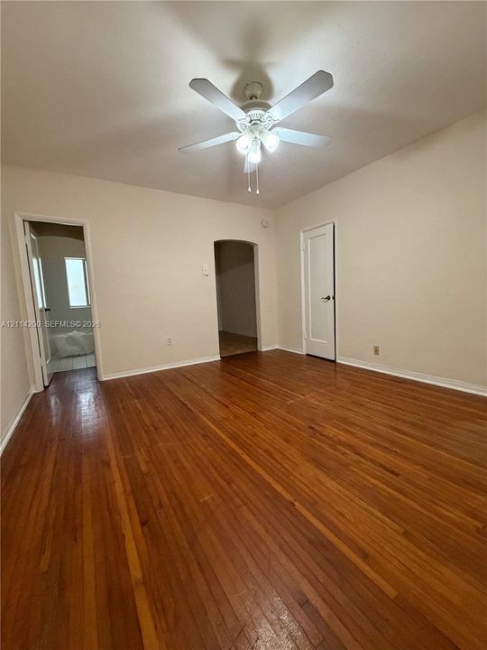 Interior space featuring wood-finish flooring, a ceiling fan with integrated lighting, a classic arched doorway, and a multi-panel interior door
