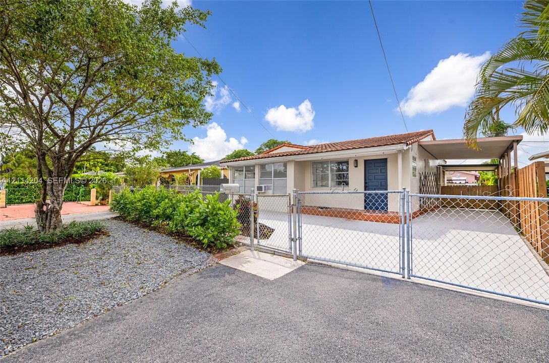 Single-story exterior featuring a tile roof, covered carport, chain-link perimeter fencing, and mature landscaping