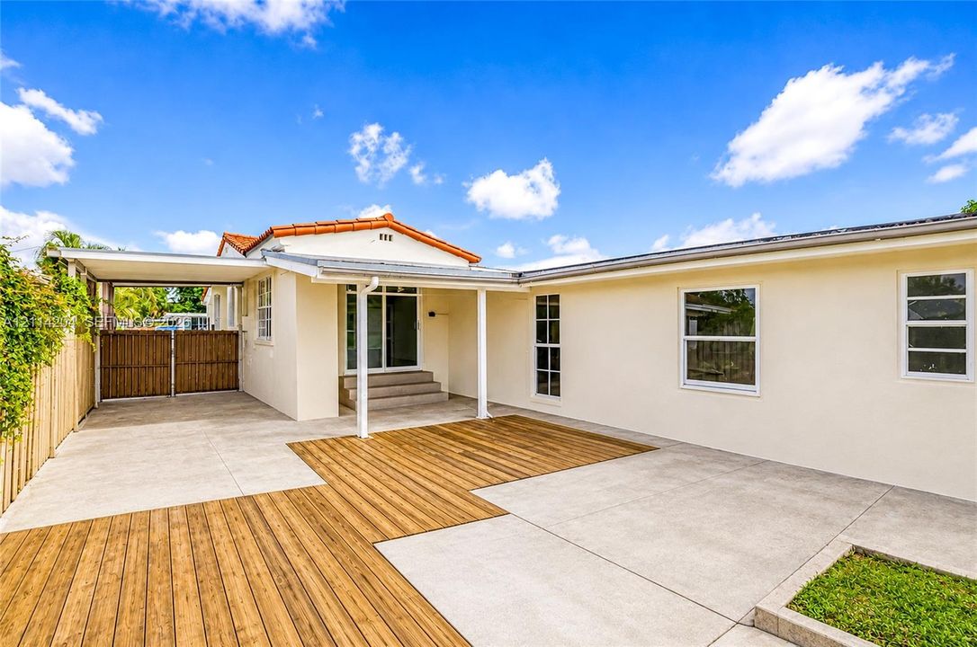 Exterior space featuring a concrete patio, integrated wood-finish decking, attached carport, and neutral stucco siding
