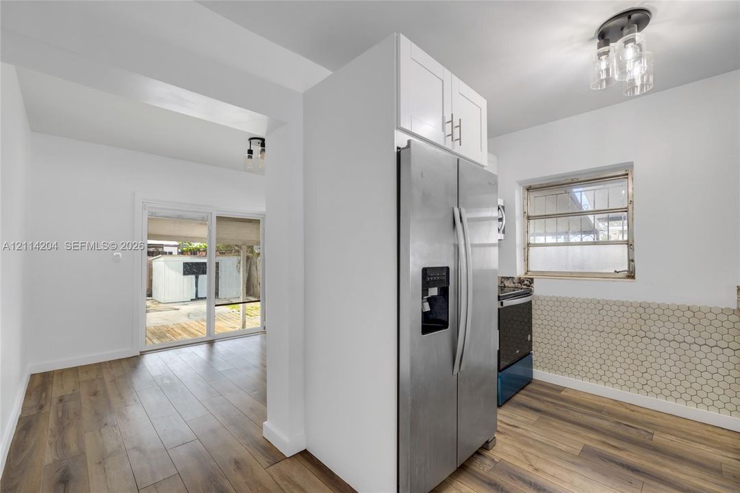 Kitchen featuring wood-finish flooring, white shaker-style cabinetry, stainless steel side-by-side refrigerator, hexagonal tile backsplash, and multi-light flush mount ceiling fixture