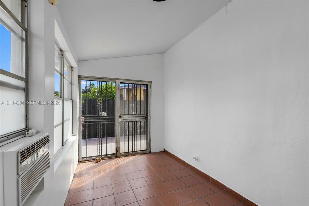 Enclosed sunroom featuring ceramic tile flooring, a mounted through-wall air conditioning unit, multiple windows, and a metal security door