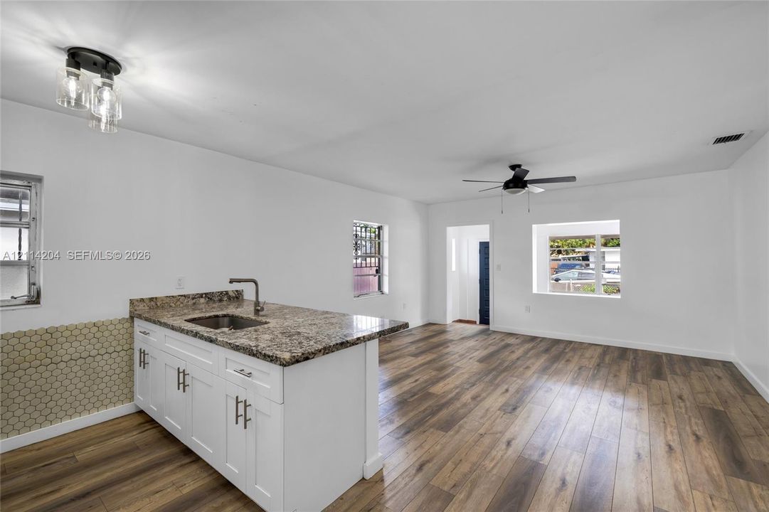 Kitchen featuring stone-finish countertops, white shaker-style cabinetry, hexagon-pattern wall tile, wood-finish flooring, and a ceiling fan