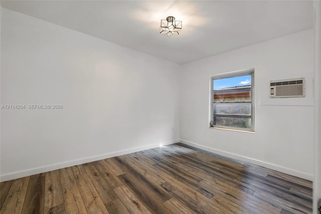 Interior room featuring wood-finish flooring, a geometric flush-mount light fixture, and a window with an integrated wall-mounted air conditioning unit