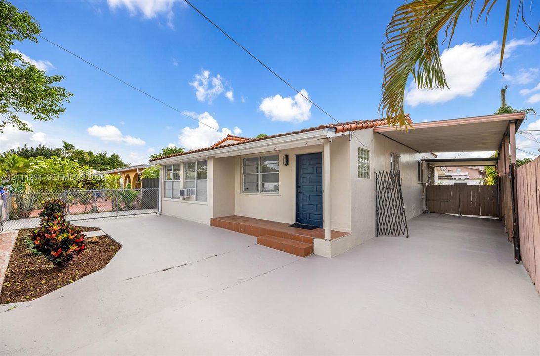 Single-story residence featuring a terracotta-tile roof, expansive concrete driveway, attached carport, and a prominent front entry with elevated porch steps
