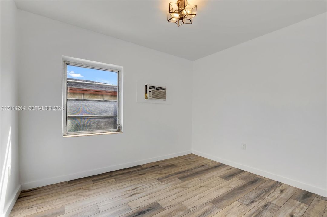 Neutral interior space featuring wood-finish flooring, a single-pane window, a built-in wall air conditioning unit, and geometric metal-frame ceiling lighting