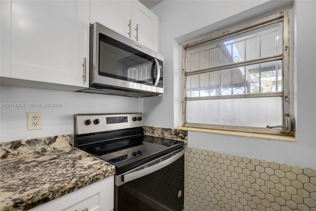 Kitchen area featuring white Shaker-style cabinetry, multi-tonal stone-composite countertops, stainless steel appliances, and a hexagonal tile backsplash
