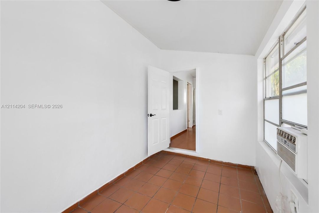 Neutral interior featuring ceramic tile flooring, a six-panel door, and a horizontal sliding window with an installed air conditioning unit