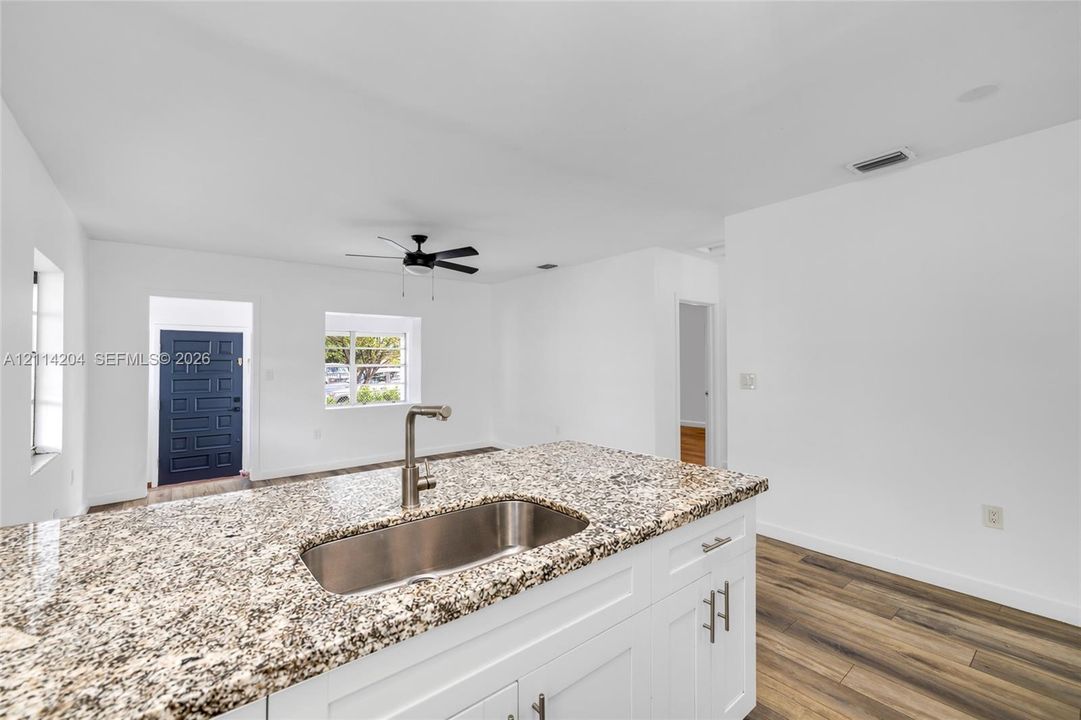 Kitchen island featuring stone-surfaced countertops, stainless steel undermount sink, gooseneck faucet, white shaker-style cabinetry, and wood-finish flooring