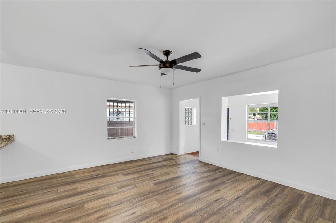 Wood-finish flooring, central ceiling fan with integrated lighting, and multiple windows providing natural light