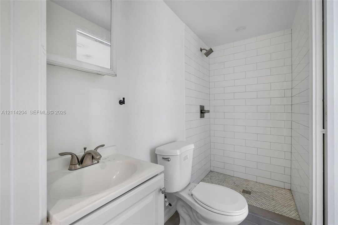 Bathroom featuring a vanity with an integrated sink, polished metal faucet, subway tile shower surround, and mosaic tile shower flooring