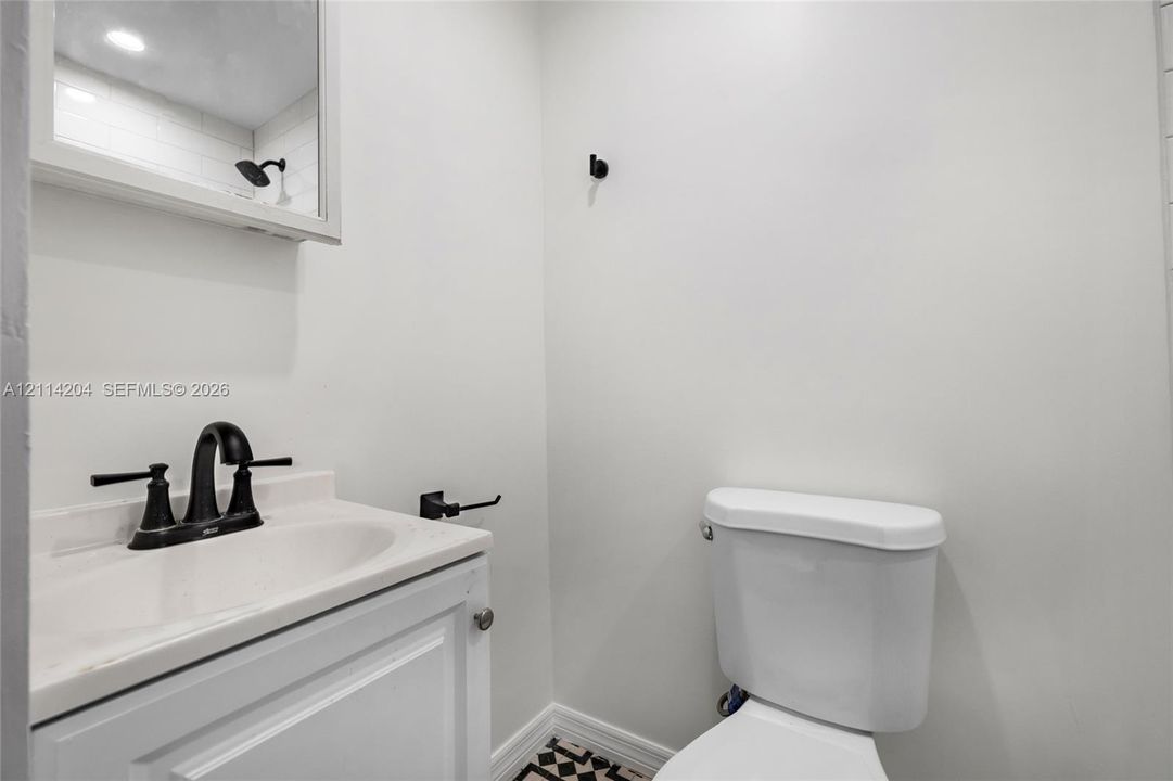 White vanity with integrated sink, matte black widespread faucet, recessed mirrored medicine cabinet, and geometric patterned floor tile