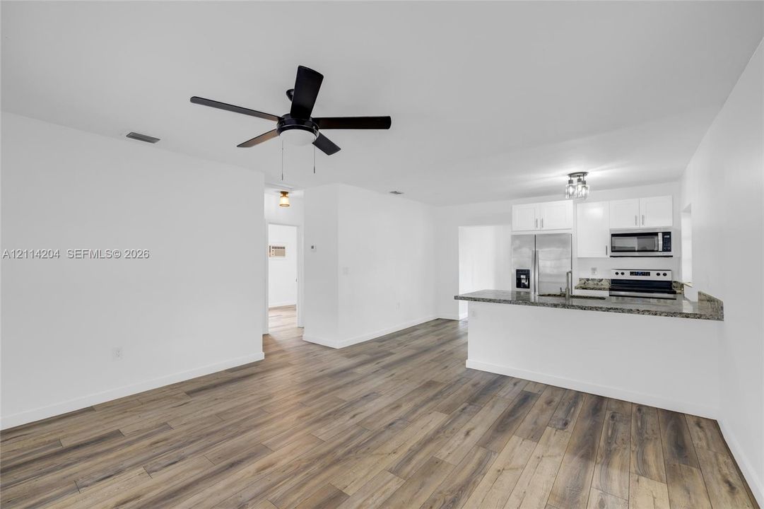 Kitchen featuring a stone-look countertop, white cabinetry, integrated microwave, and wood-finish flooring, complemented by a ceiling fan