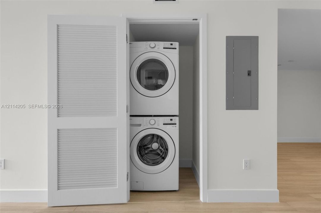 Laundry closet featuring a white louvered door and stacked white appliance set