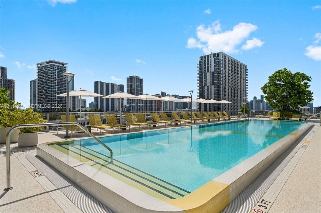 Rooftop swimming pool featuring a tiled basin, integrated step entry, textured perimeter decking, and stainless steel handrails