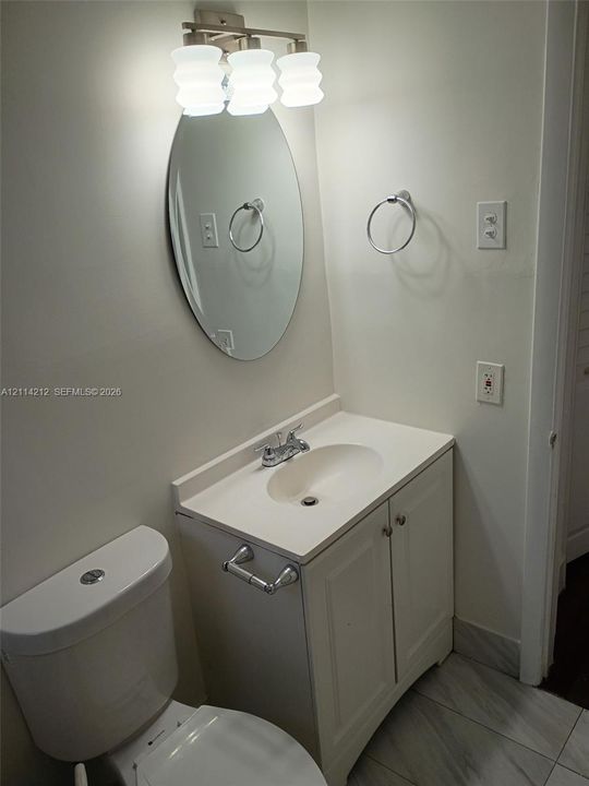 Bathroom featuring a white vanity cabinet with a integrated basin, oval wall-mounted mirror, three-light fixture, and stone-finish tile flooring