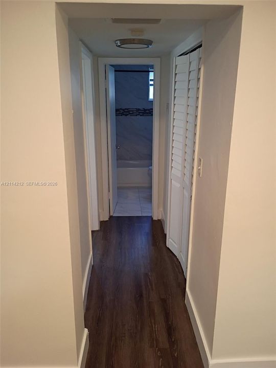 Hallway featuring wood-finish flooring, white louvered-style bi-fold closet doors, and a flush-mount ceiling light fixture