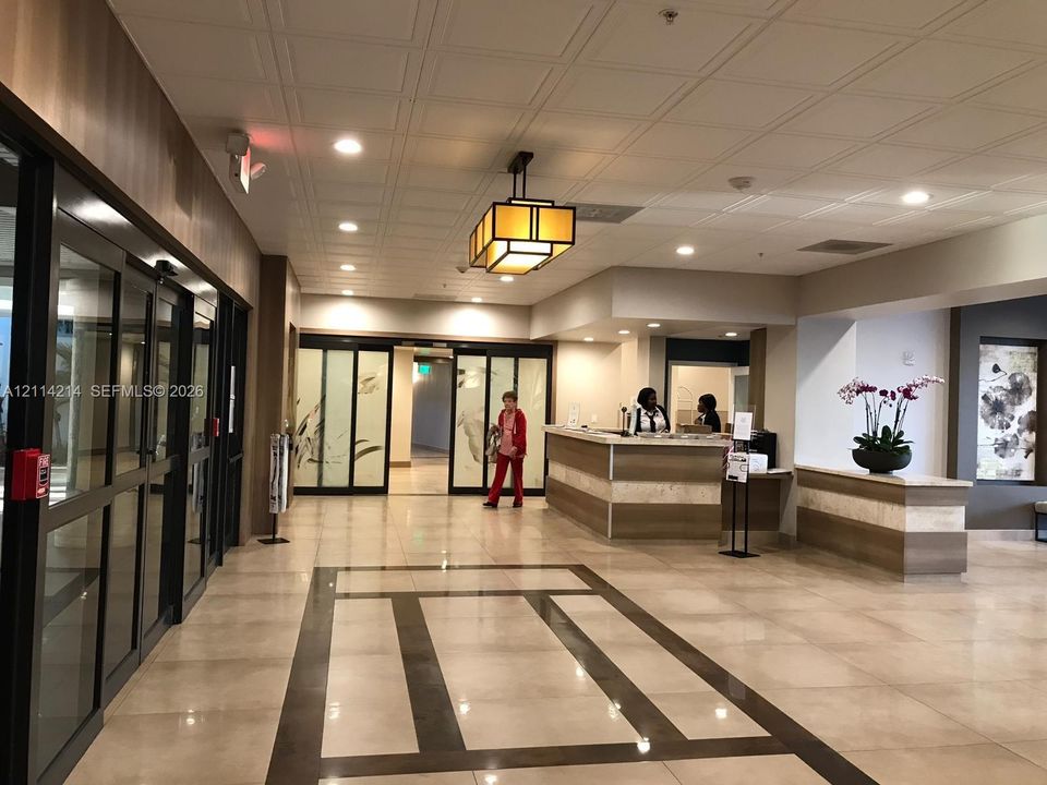 Lobby featuring tile flooring with decorative stone inlay, coffered ceiling, custom reception desk with stone detailing, glass-paneled sliding entry doors, and geometric mission-style pendant lighting