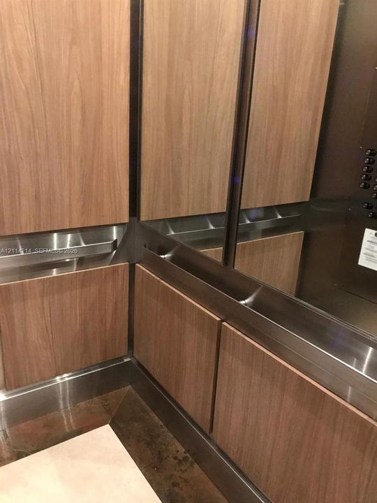 Elevator interior featuring wood-finish paneling, brushed metallic trim, and integrated stainless steel handrails